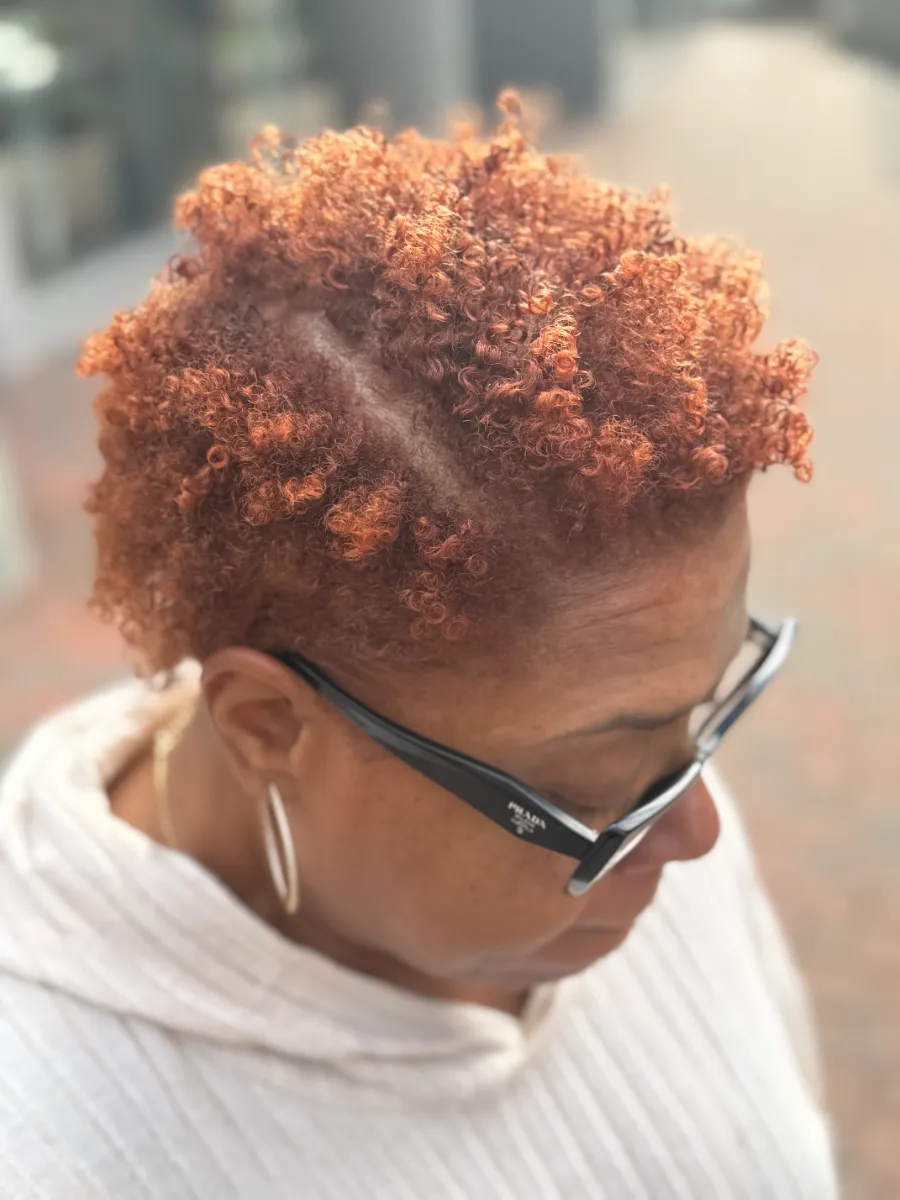 A guest's tapered short curls colored bright copper and styled into defined coils, with a shaved side part, outdoors in daylight