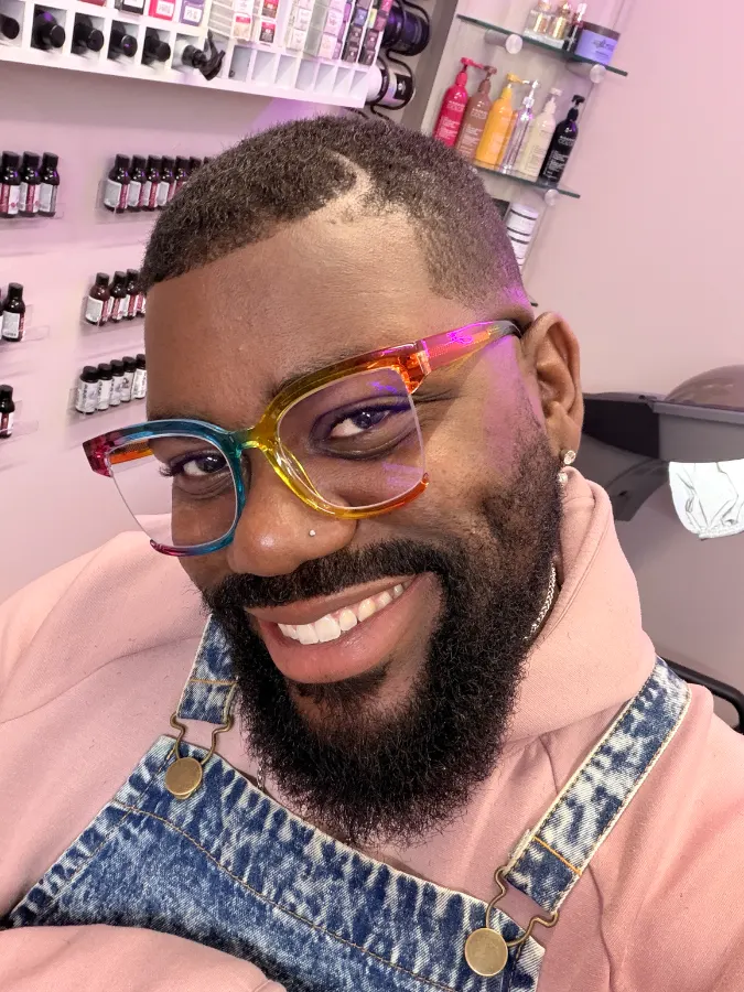 Victor with his natural dark, close-cut hair and a sharp hairline, smiling in rainbow glasses