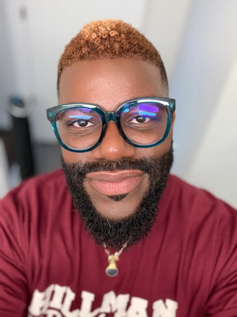 Victor Anthony Scotti, Jr., short hair colorist, smiling in teal glasses, his short curls colored warm copper