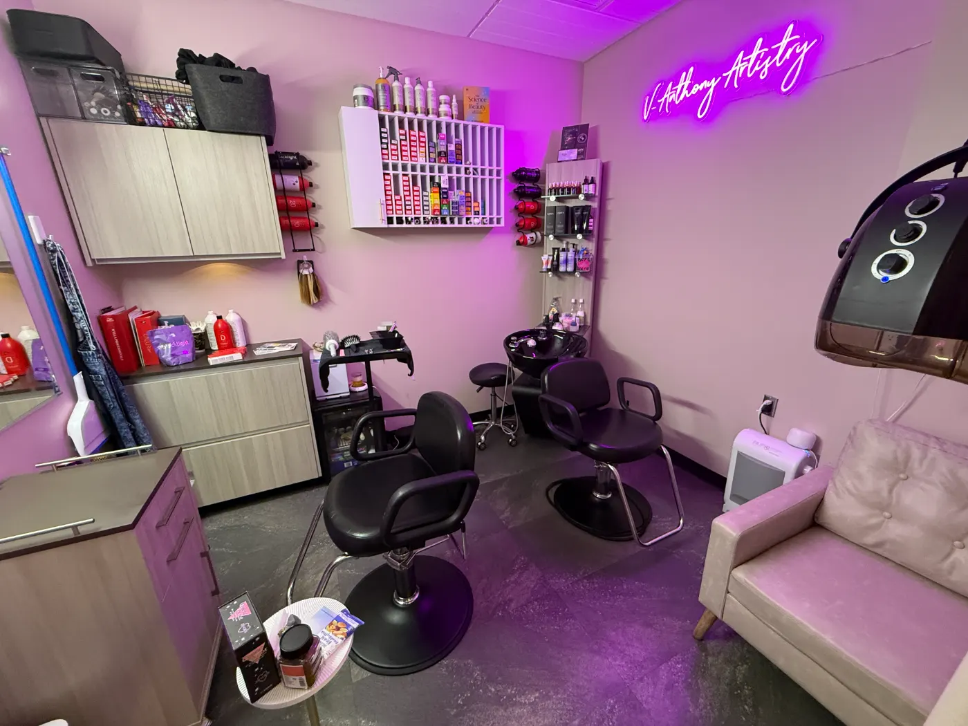 Victor's private suite at Sola Salon Studios Arlington: styling chairs, a shampoo bowl, a wall of color tubes and a pink sofa under a violet neon sign