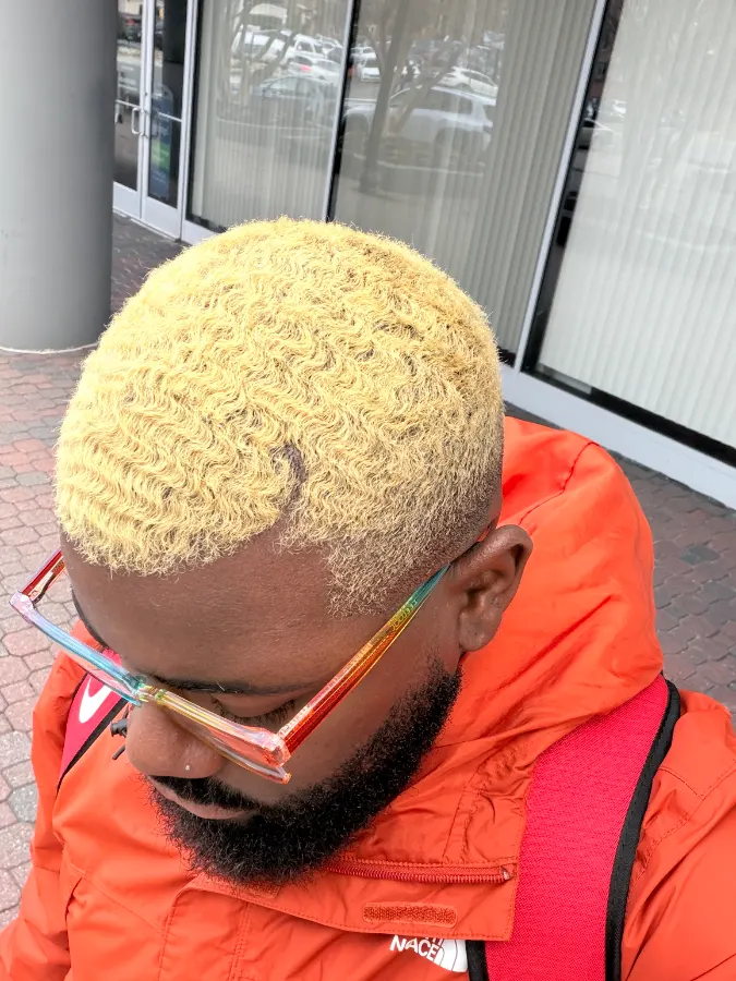 From above: Victor’s short waves lightened to a bright yellow blonde, cut close at the sides, outdoors
