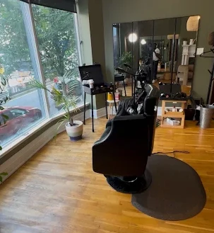 The styling chair at XP Studio DC, facing a tall window onto the street, with a potted palm and a color cart beside it